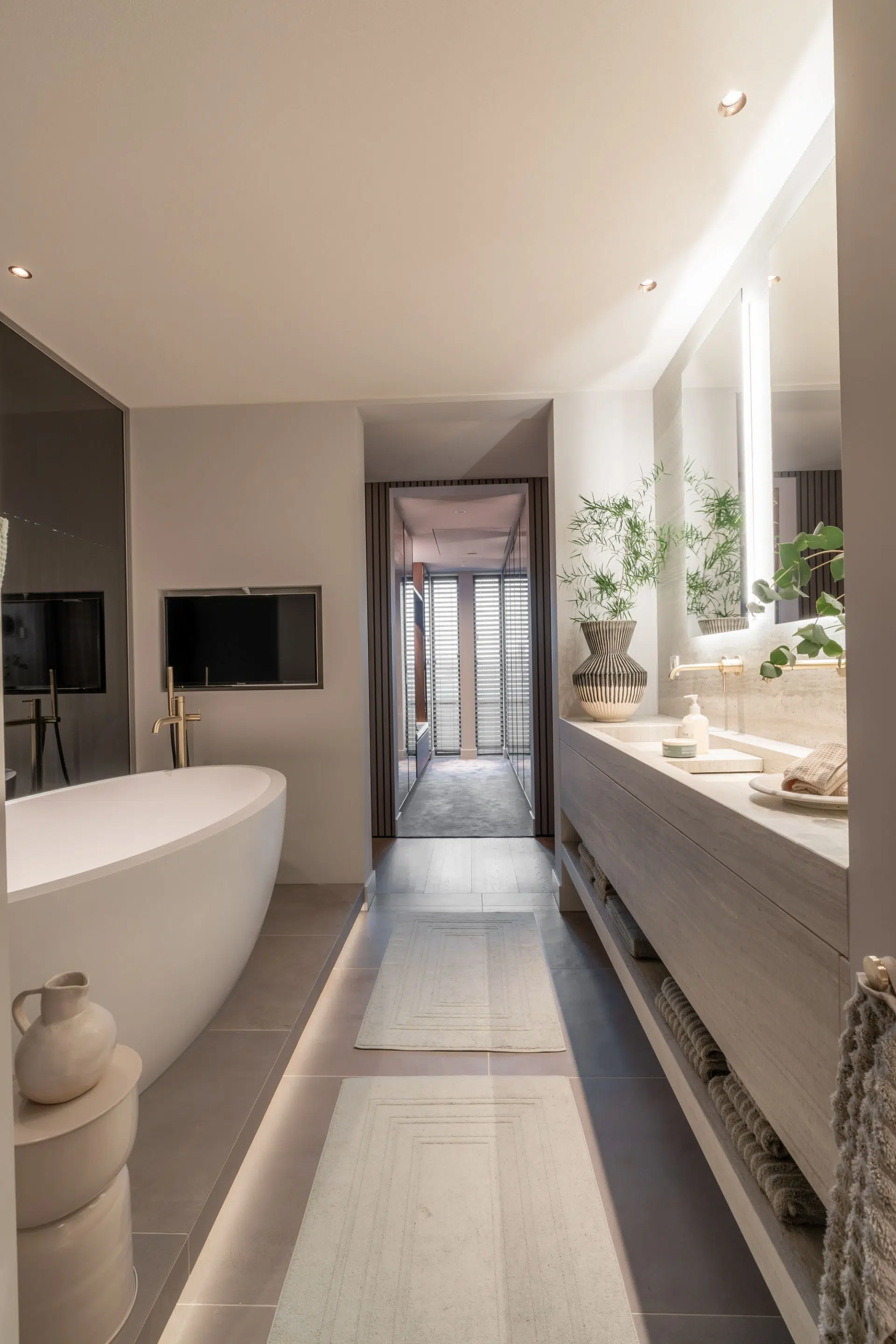 Vrijstaand ligbad, maatwerkwastafel, luxe maatwerk spiegel met verlichting, Gessi wastafelkranen geborsteld brons, beige badkamer