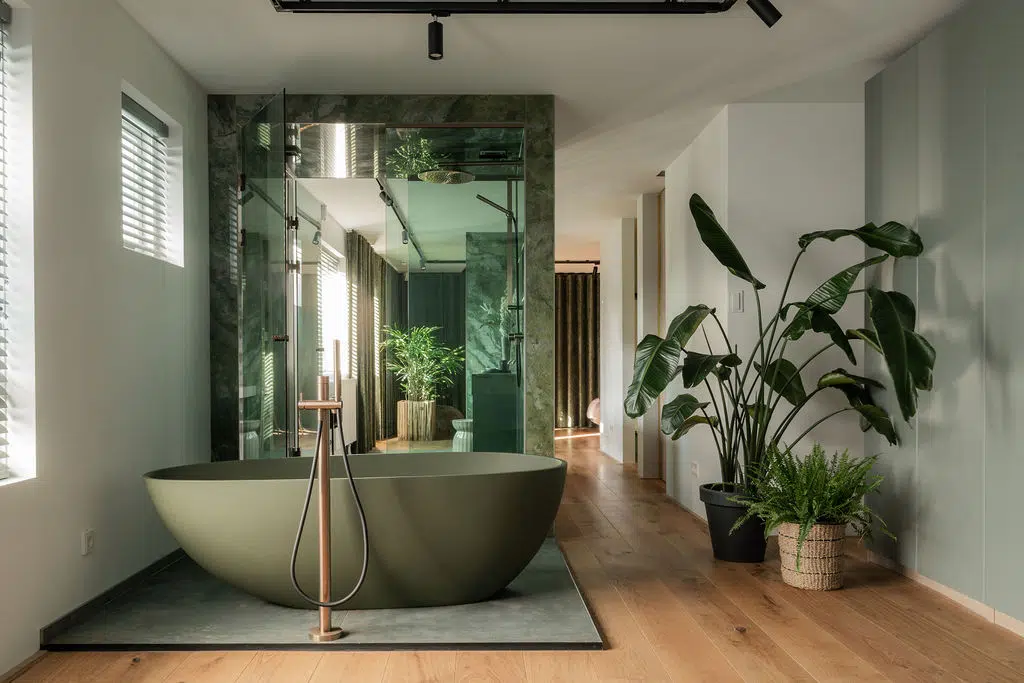 Impressie van een design badkamer in ensuite stijl. De badkamer is geplaatst in een open ruimte, met veel glaswerk, en tegels, een bad en een glazen douchewand in groen.
