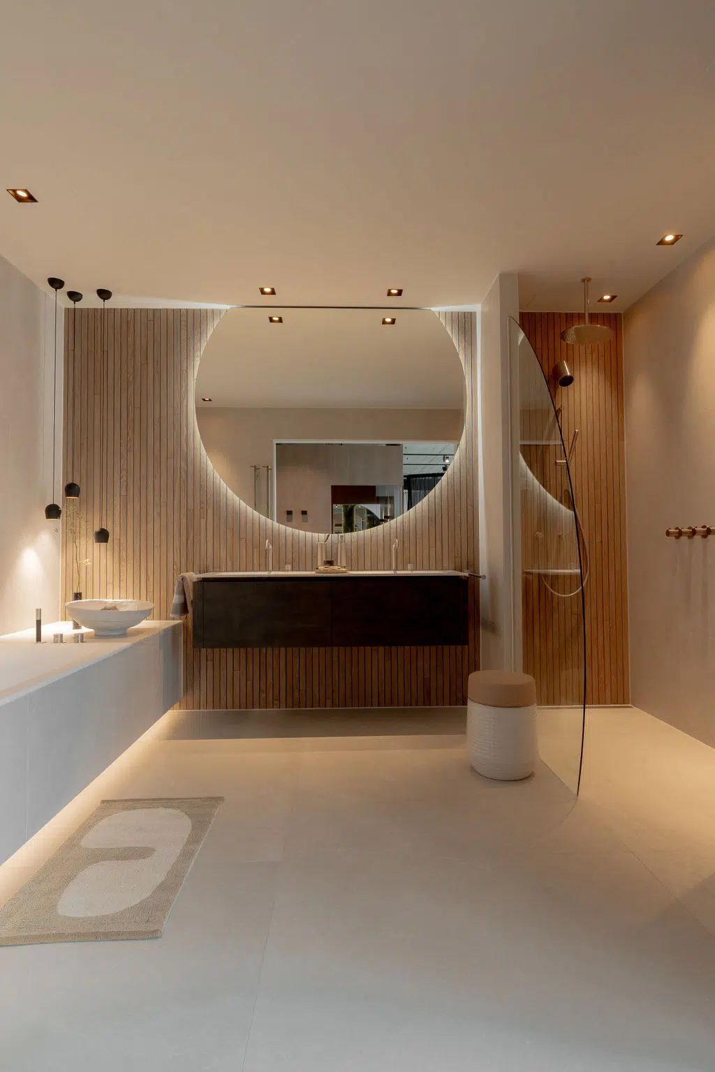 Impressie van een Japandi badkamer, voorzien van neutrale tegels, custom houtlook badkamertegels, een zwevend badkamermeubel, glazen douchewand, grote spiegel met verlichting en rvs badkamerkranen.