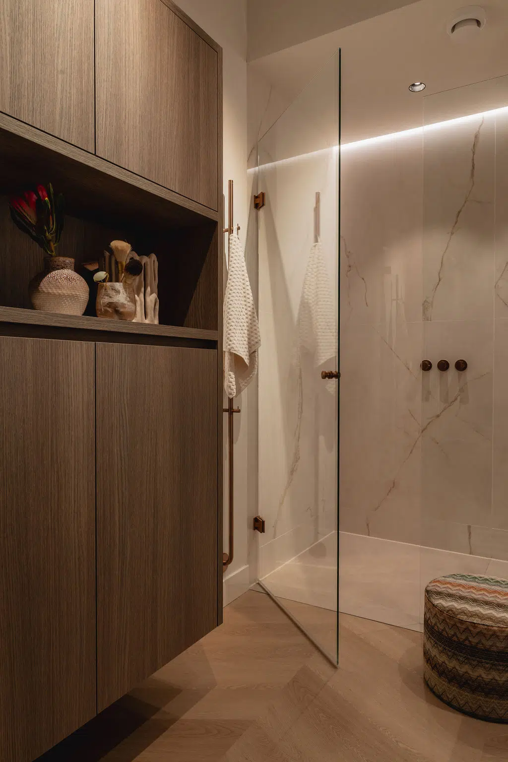 Impressie van een kleine badkamer met een zwevende badkamerkast van donker hout en douche met glazen douchedeur.