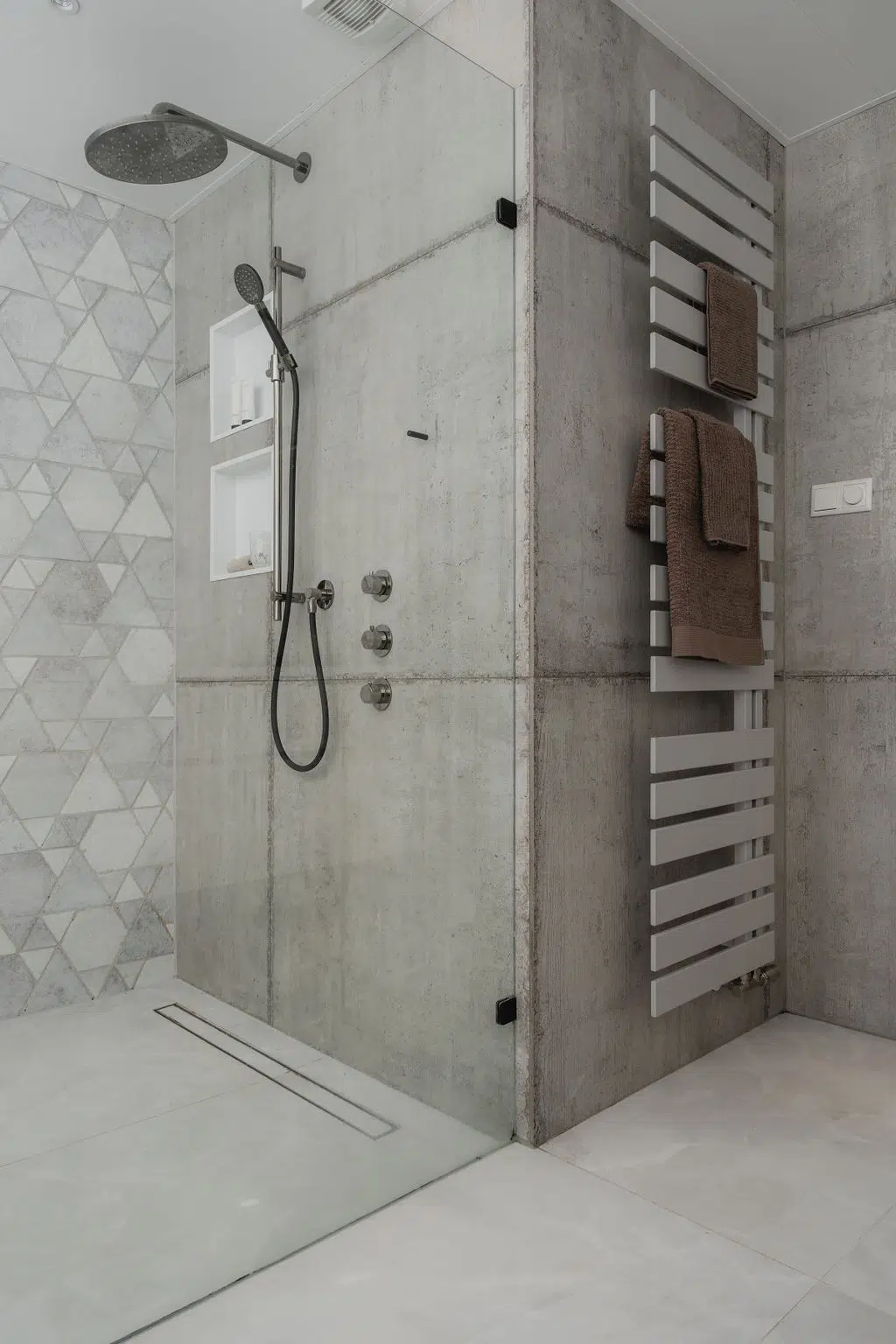 Impressie van een moderne badkamer, voorzien van driehoek tegels, een douche met nis, zwart chroom kranen, glazen douchewand en een designradiator.