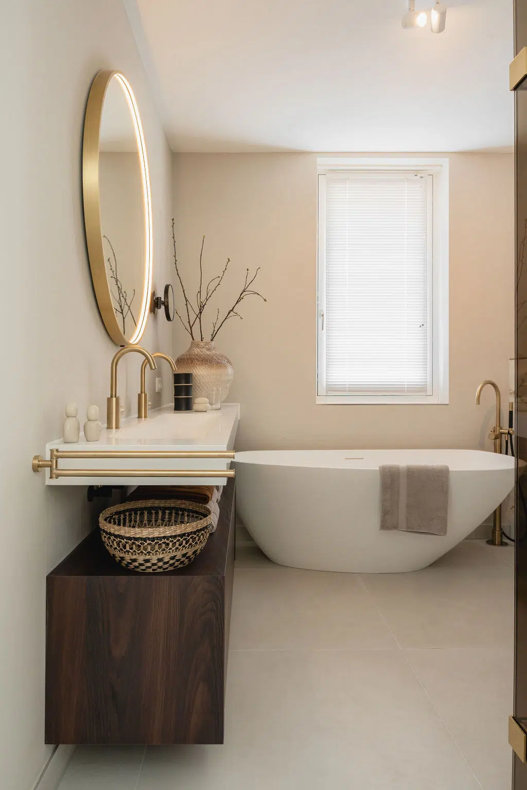 Impressie van een luxe badkamer met rustige kleuren als basis. De badkamer is ingericht met een organisch gevormd bad, gestucte wanden, kranen in geborsteld messing en notenhout badkamermeubel.