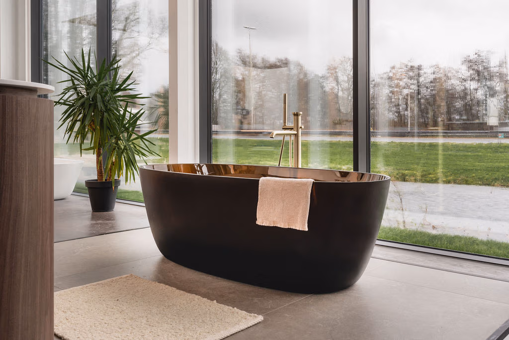 Impressie vanuit de showroom van De Eerste Kamer Badkamers, waar we kijken naar een donkerkleurig en glanzend vrijstaand bad met rondgevormde Gessi vloerkraan.